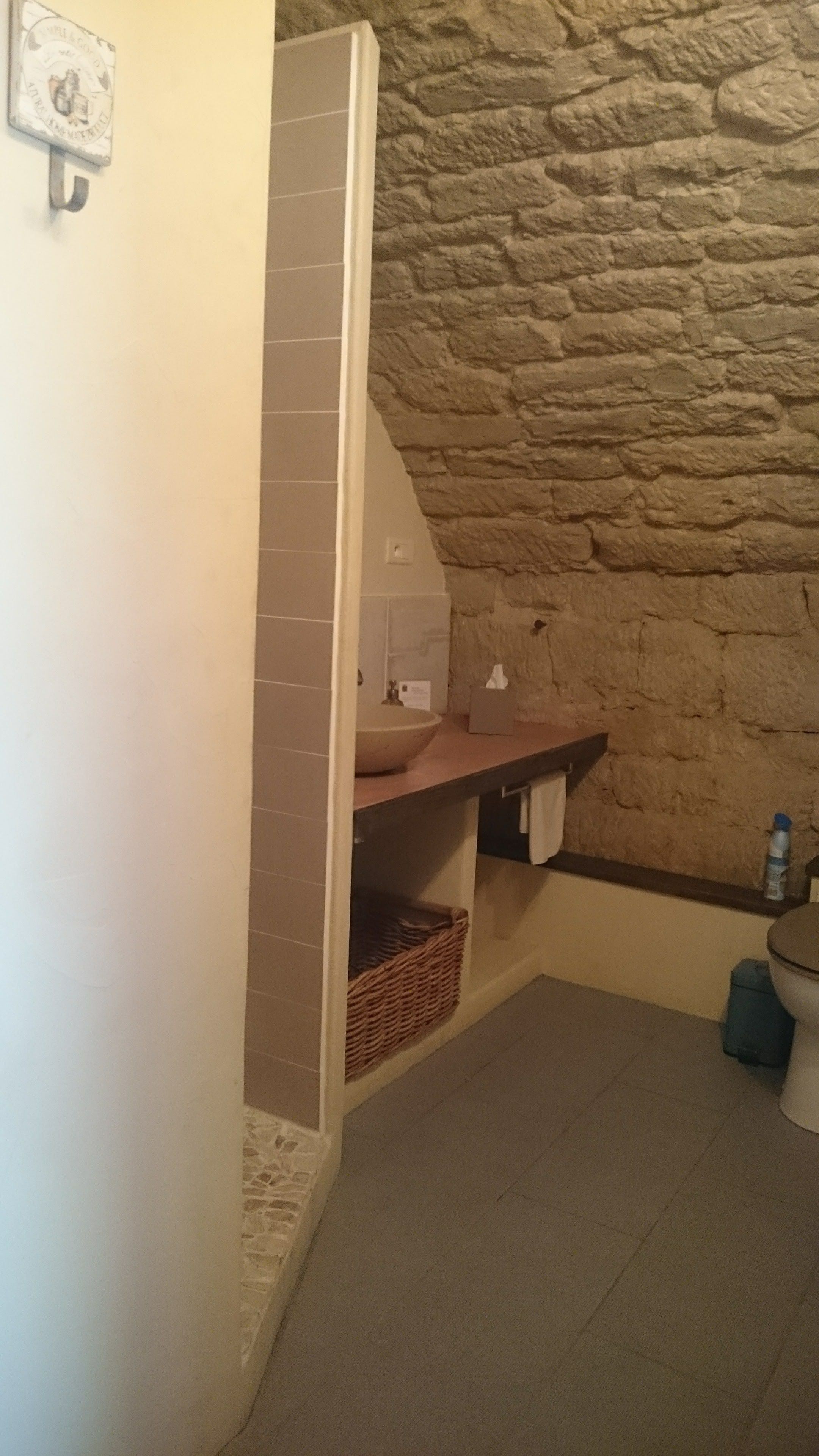 Een badkamer met een stenen muur, een wastafel, een handdoekhouder en een toilet.