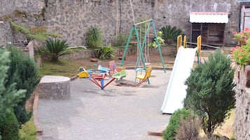 Children can play on swings, a slide, and a seesaw in this outdoor play area surrounded by a garden.