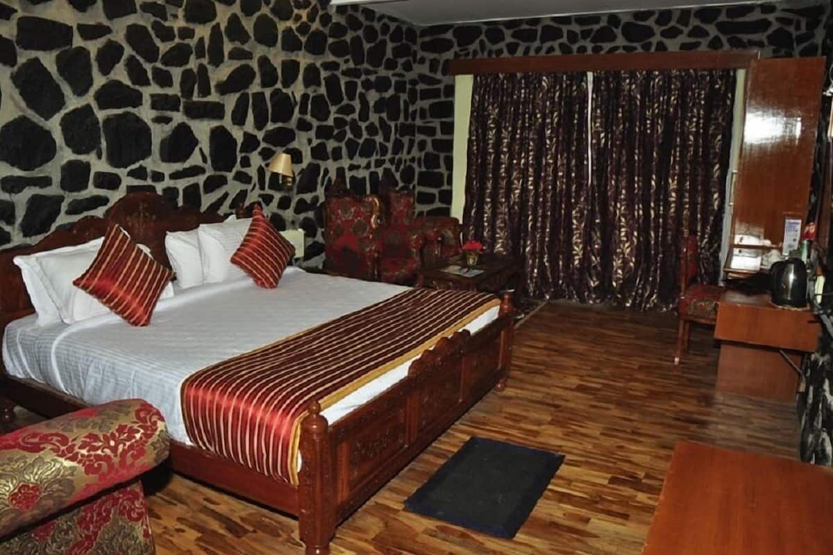A large bed with multiple pillows, a wooden headboard, and a stone wall.