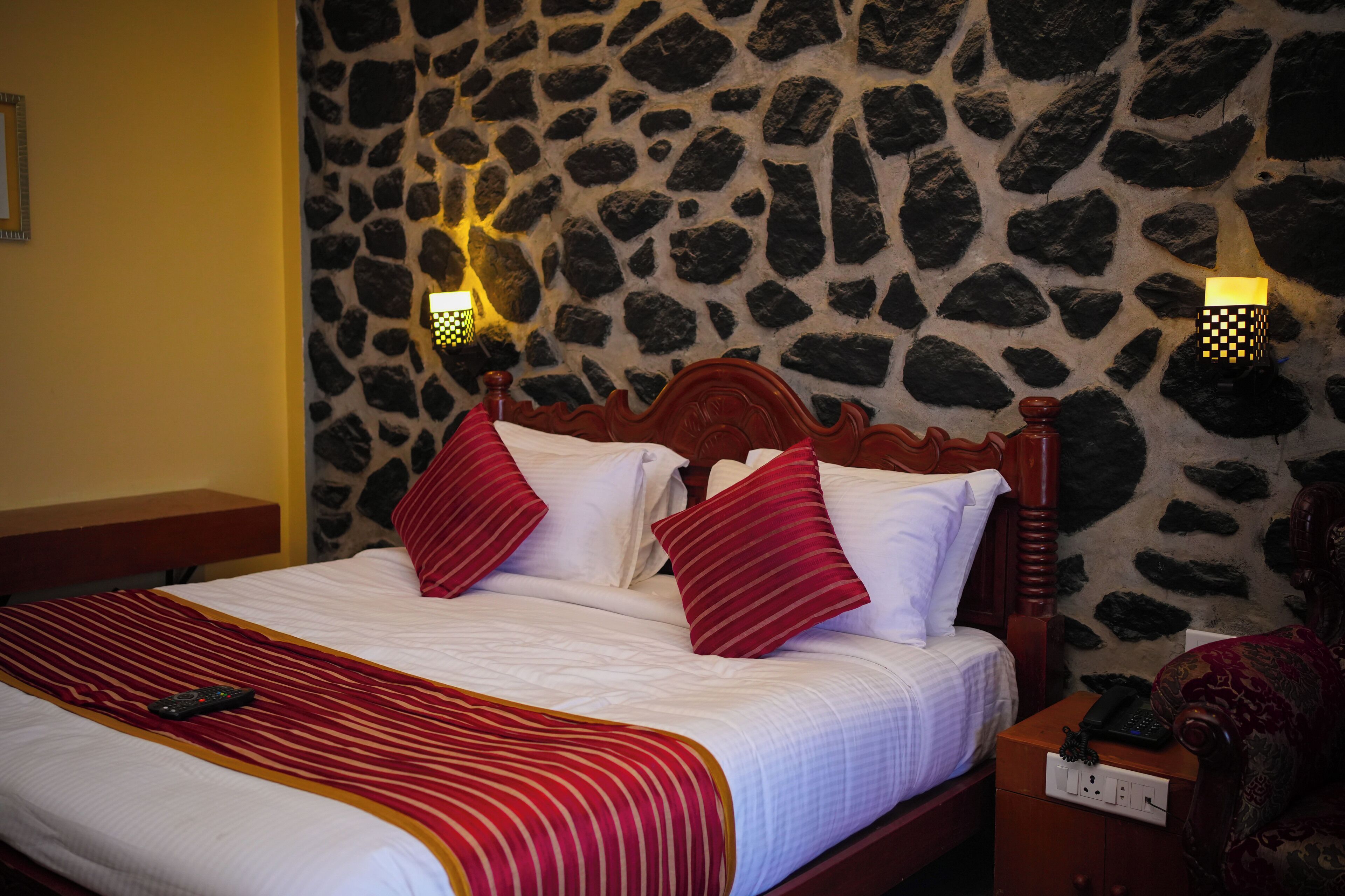 A bed with a wooden headboard, white bedding, and red striped pillows. There are two wall-mounted lights on either side of the bed.