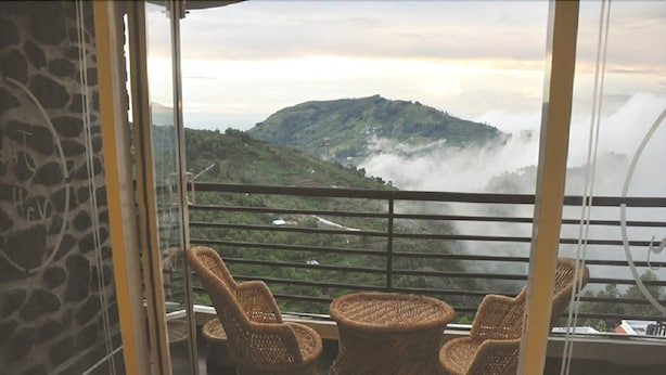 A balcony with wicker chairs and a view of a mist-covered mountain. - Jem Valley (Kodaikanal)