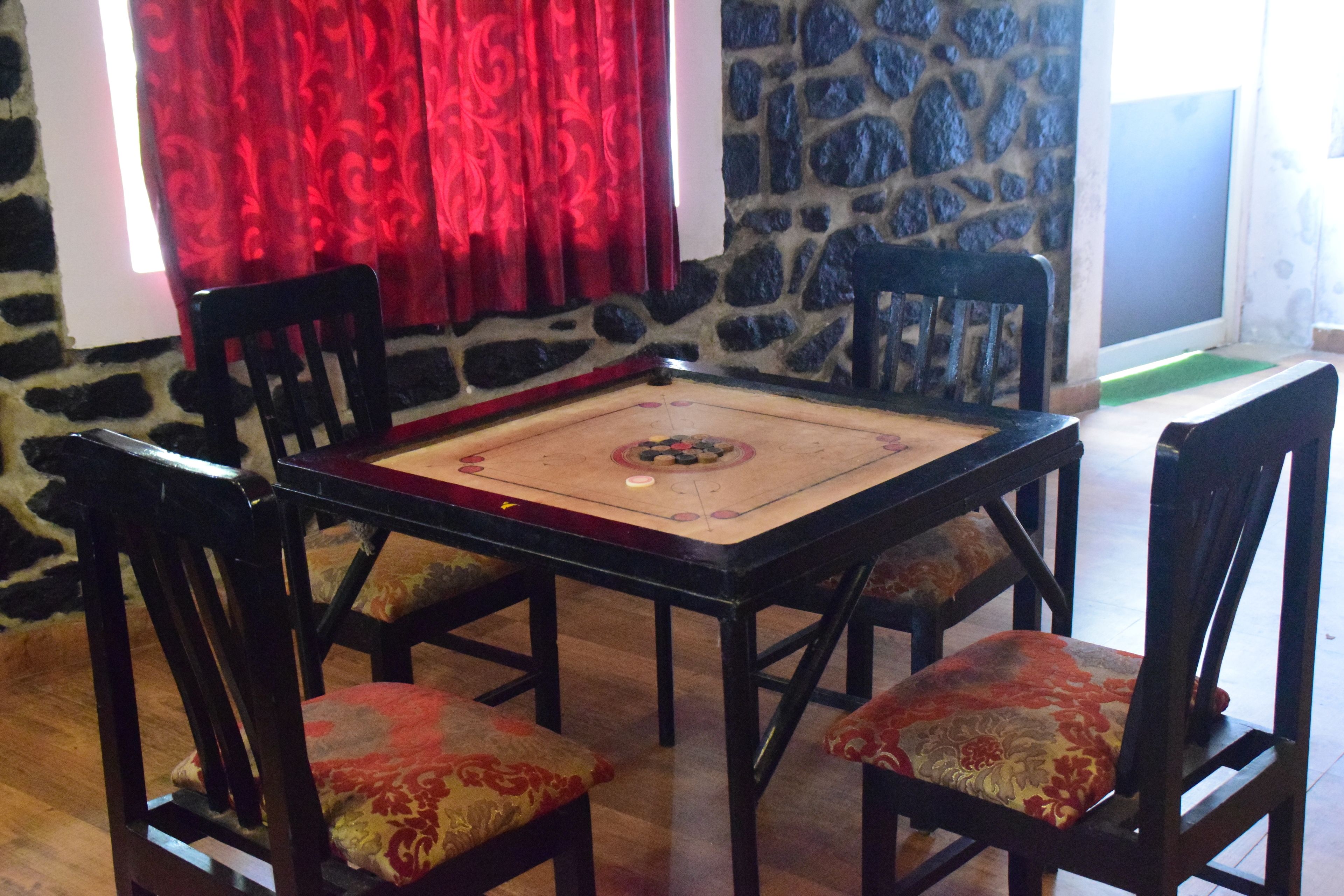 A room with a stone wall, a red curtain, a table with a patterned tablecloth, and four chairs with cushioned seats.