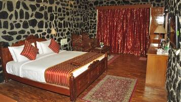 Un dormitorio con una cama grande, un cabecero de madera, una pared de piedra, una cortina roja, un escritorio con una lámpara y una alfombra.
