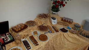 Taula de buffet amb diferents postres i aperitius, una torradora i un ram de flors vermelles.