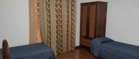 Una habitación con dos camas individuales, un armario de madera y una cortina con motivos florales.