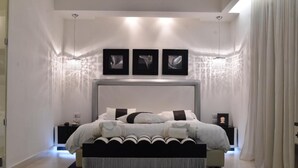 Une chambre à coucher moderne avec un grand lit, une tête de lit, des tables de chevet et trois tableaux encadrés accrochés au mur.