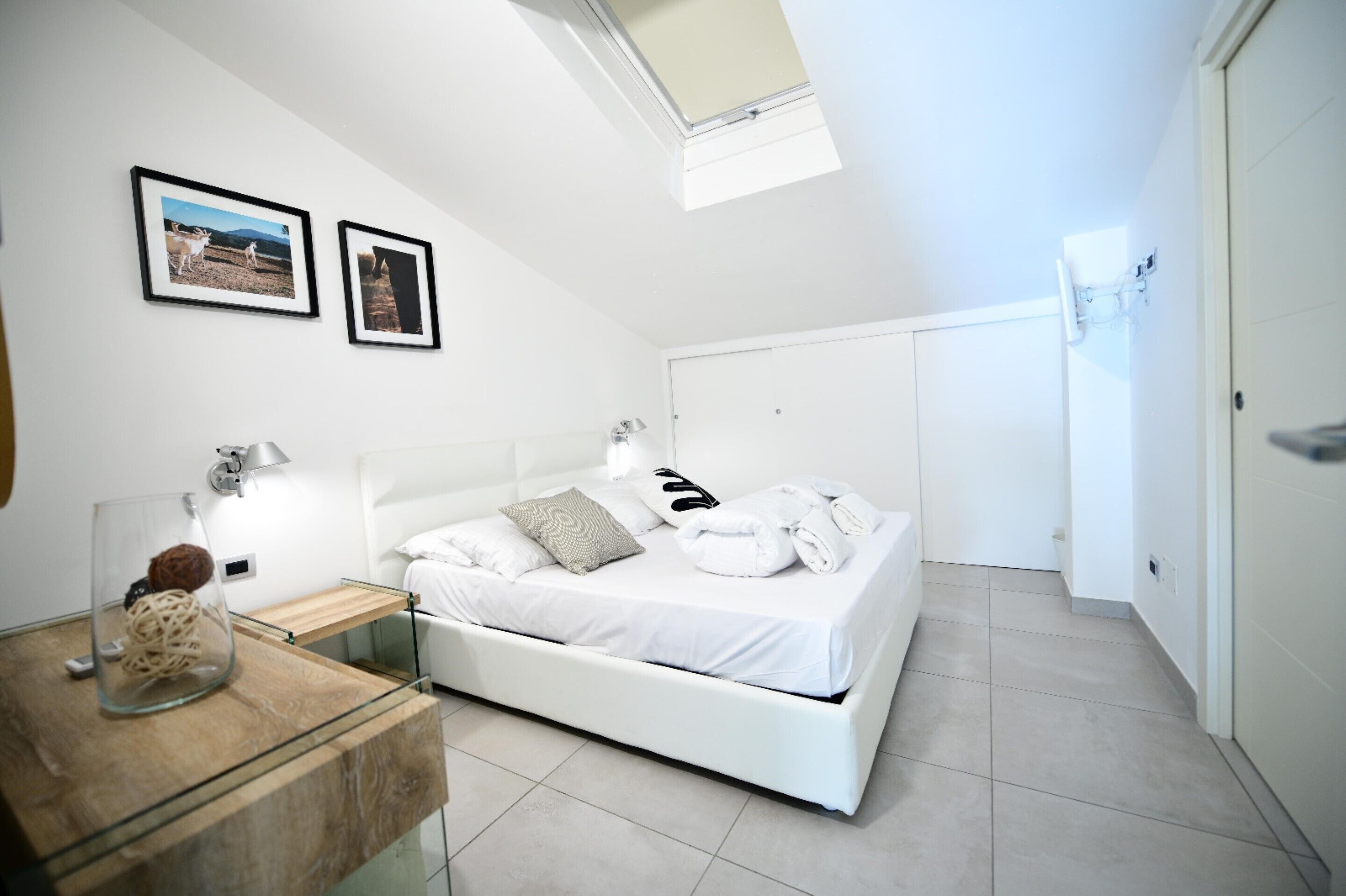 Een moderne slaapkamer met een bed, nachtkastjes, een glazen salontafel en afbeeldingen in lijsten aan de muur.