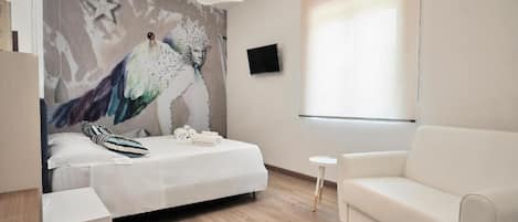 Un dormitorio moderno con una cama, un sofá blanco, una mesita y un televisor instalado en la pared.