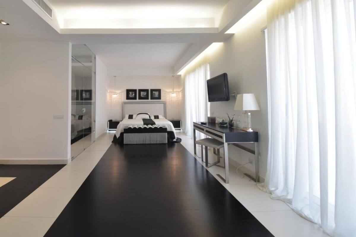 Una habitación de hotel moderna con una cama grande, un escritorio con computadora, un televisor y un ventanal con cortinas.