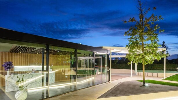 Un bâtiment moderne doté d’un comptoir d’accueil, de murs en verre et d’un espace extérieur bien éclairé, agrémenté d’un arbre.