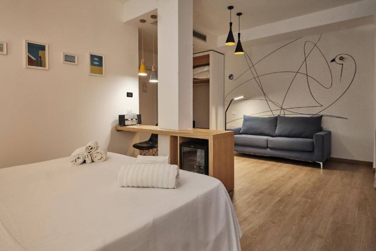 Un dormitorio moderno con una cama grande, un escritorio pequeño, un sofá gris y suelo de madera.