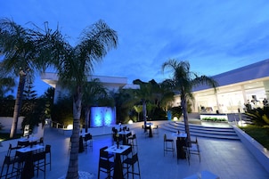 An outdoor dining area with tables and chairs, palm trees, and a water feature.