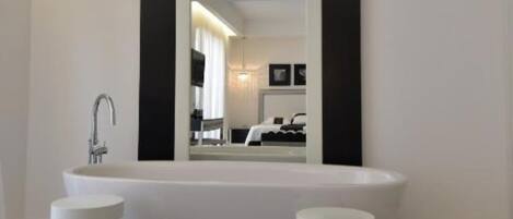 Un baño moderno con una bañera independiente, un espejo grande y dos taburetes blancos.