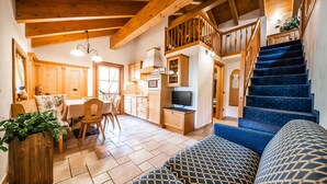 A cozy living area with a staircase, wooden beams, a dining area, and a kitchen. - Chalet Mottolino (Livigno)