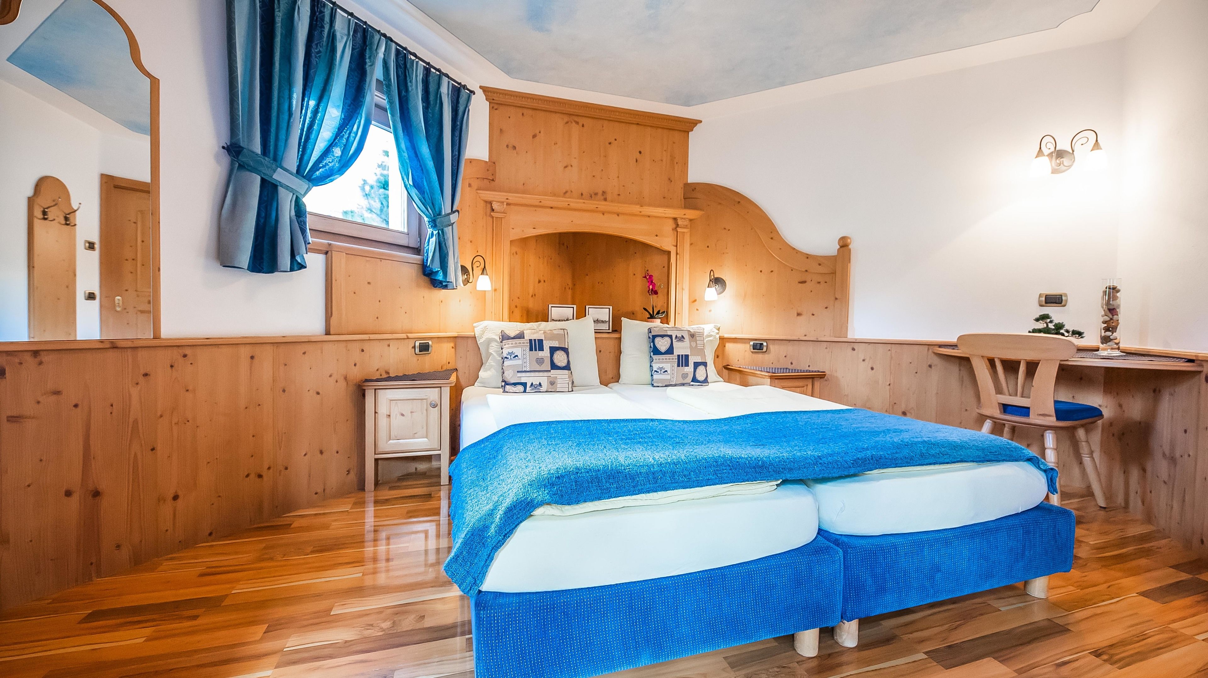 Une pièce aux murs lambrissés, avec un grand lit, un petit bureau et une chaise.