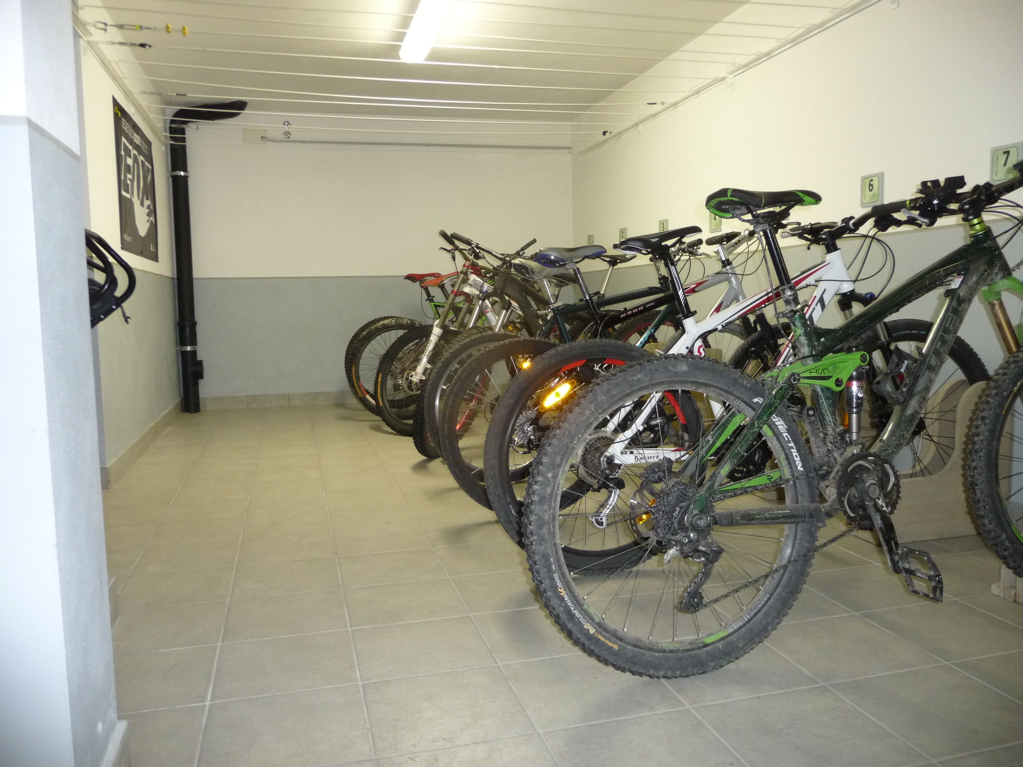 A bike parking area with multiple bicycles, a tiled floor, and a white ceiling with fluorescent lighting.