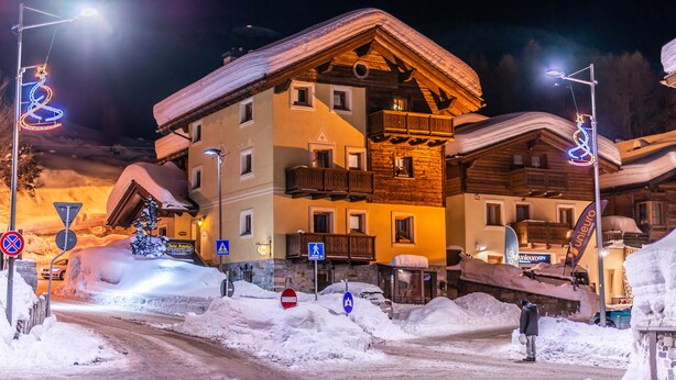 A multi-story building with balconies, a snow-covered roof, and a sign indicating a ski resort. - Chalet Mottolino (Livigno)