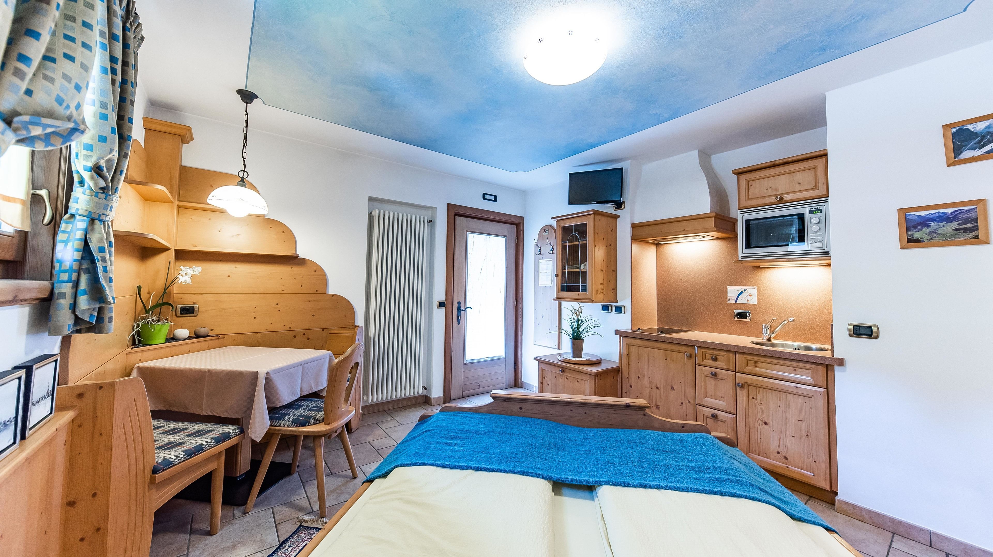 Ein kleines Zimmer mit einem Bett, einem Tisch, einem Stuhl, einer Küchenzeile und einer Tür.
