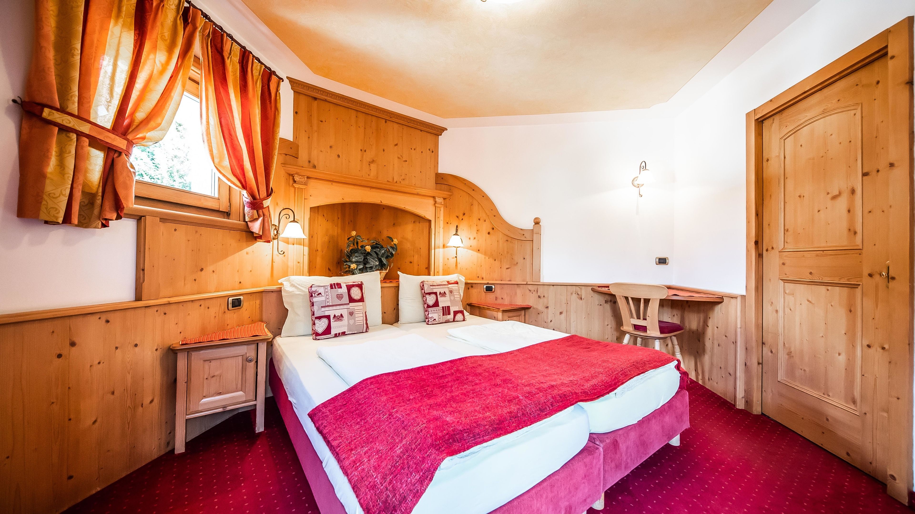 A wooden-paneled bedroom with a bed, nightstands, a desk, and a chair.