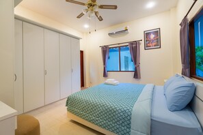 Un dormitorio con cama, armario, aire acondicionado, ventilador de techo y ventana con cortinas.