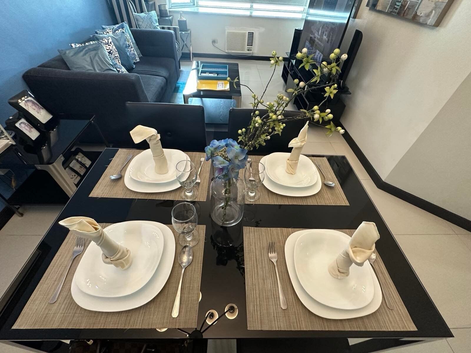Une table à manger dressée avec de l’argenterie, des assiettes blanches et un vase rempli de fleurs.