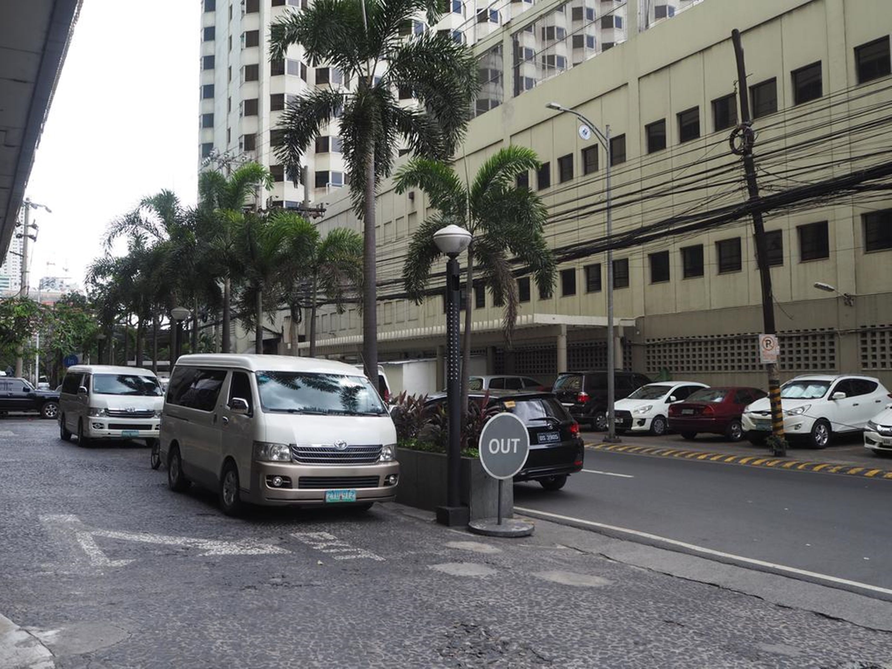 Una calle con vehículos estacionados, un cartel de 'No Estacionar' y un edificio de varios pisos y balcones.