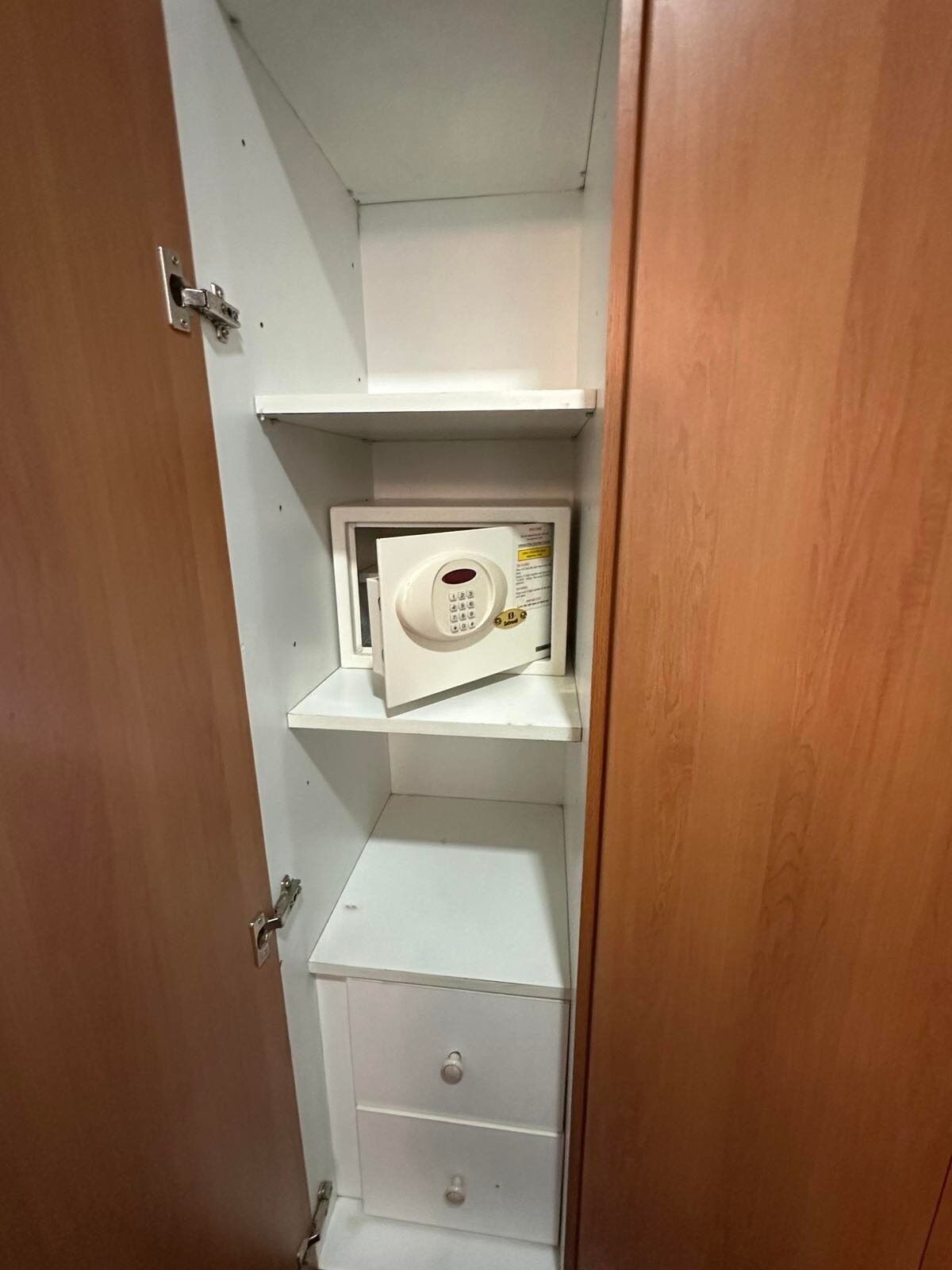 Un espacio reducido y cerrado con un microondas en un estante, una puerta con picaporte y un cajón debajo.
