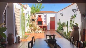 A dining area with a long table and chairs, a stone oven, and potted plants. - La Posá (La Nava de Santiago)