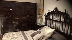 A bedroom with a large dark wooden wardrobe, a bed with patterned bedding, a nightstand with a lamp, and a painting on the wall. - La Posá (La Nava de Santiago)