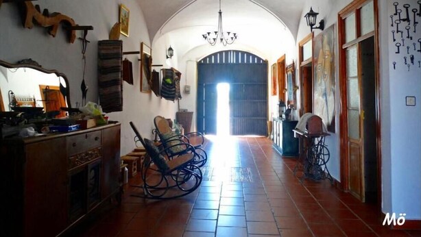 A spacious hallway with a high ceiling, a chandelier, and a view into a room with a large window. - La Posá (La Nava de Santiago)