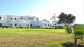 Un edificio blanco con varias ventanas y techo plano, rodeado de césped y algunos árboles.