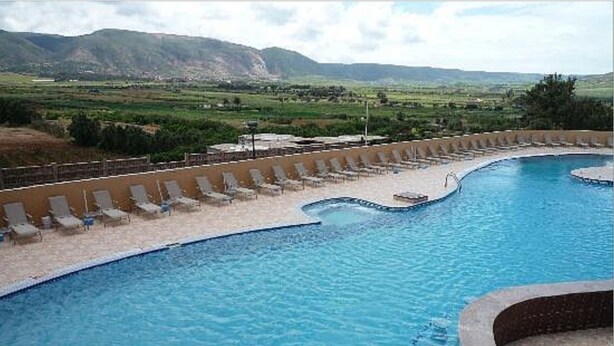 Una piscina de diseño curvo, rodeada de sillones de descanso y vistas a montañas distantes.