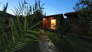 A rustic cabin with a wooden exterior, a visible window, and a pathway leading to the entrance. - Emek Pansiyon (Kemer)