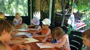 A group of children engaged in a drawing activity at a wooden table outdoors. - Emek Pansiyon (Kemer)