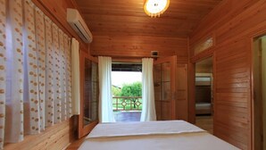 A wooden cabin room with a bed, a window with curtains, and an air conditioning unit. - Emek Pansiyon (Kemer)