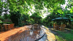 A wooden deck with outdoor furniture, surrounded by lush greenery and trees. - Emek Pansiyon (Kemer)
