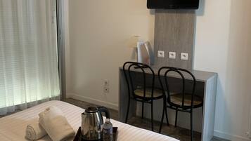 A hotel room with a bed, a desk with two chairs, a flat-screen TV mounted on the wall, and a window with curtains.