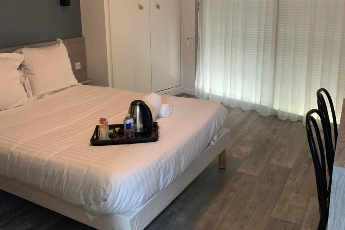 A hotel room with a bed, bedside table, and a window with curtains.