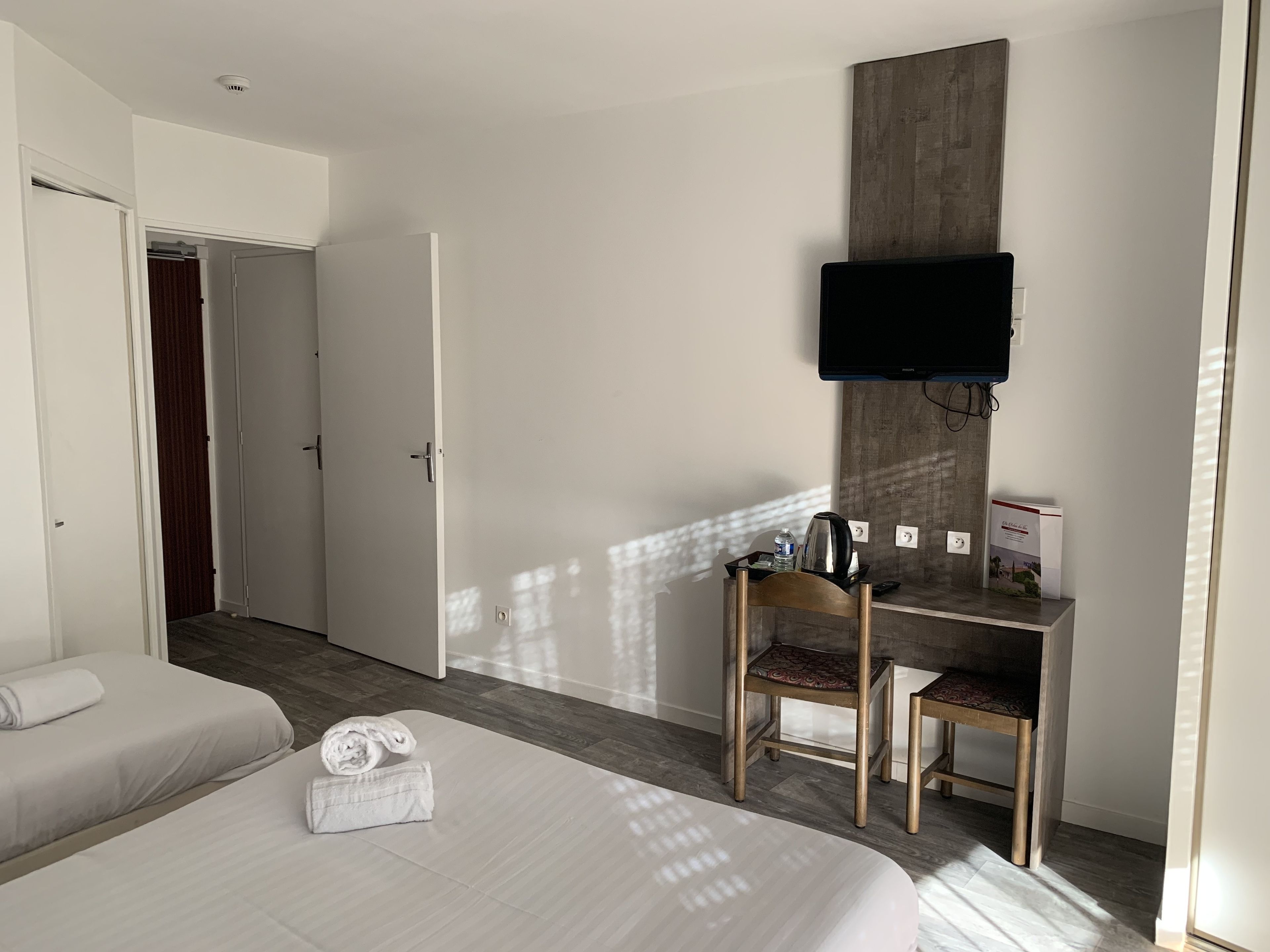 A hotel room with a bed, a desk with a chair, a television, and a wardrobe.