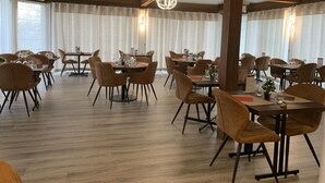 A spacious dining area with wooden beams, tables set with chairs, and large windows with curtains. - Relais des Lilas (Parthenay)