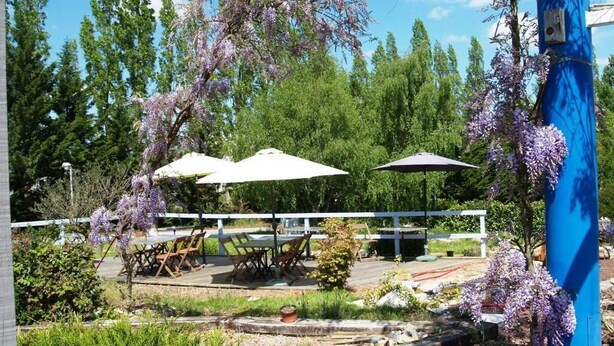 An outdoor seating area with tables and umbrellas, surrounded by lush greenery and flowering trees. - Relais des Lilas (Parthenay)