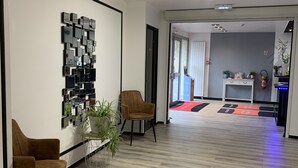 A modern office space with a reception area, two brown chairs, a wall-mounted light fixture, and a wooden floor. - Relais des Lilas (Parthenay)