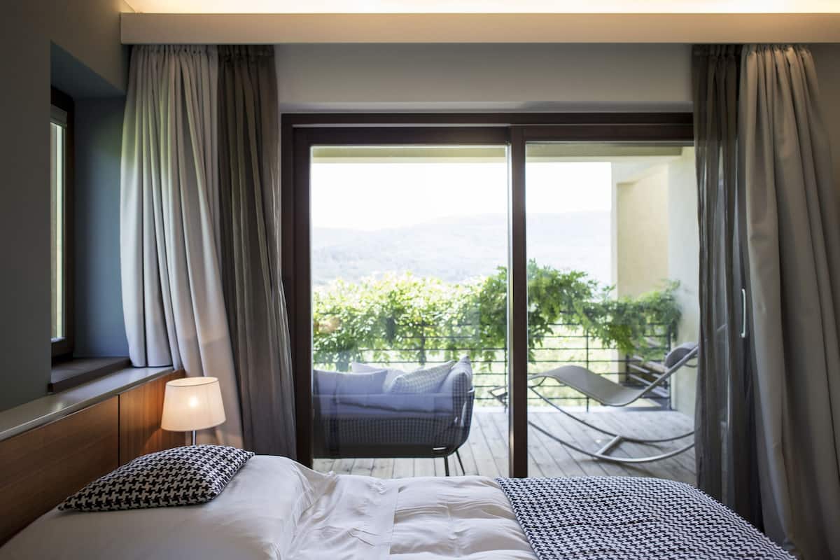 Une chambre d’hôtel avec un lit, une lampe et une vue sur un balcon extérieur agrémenté de chaises et de plantes.