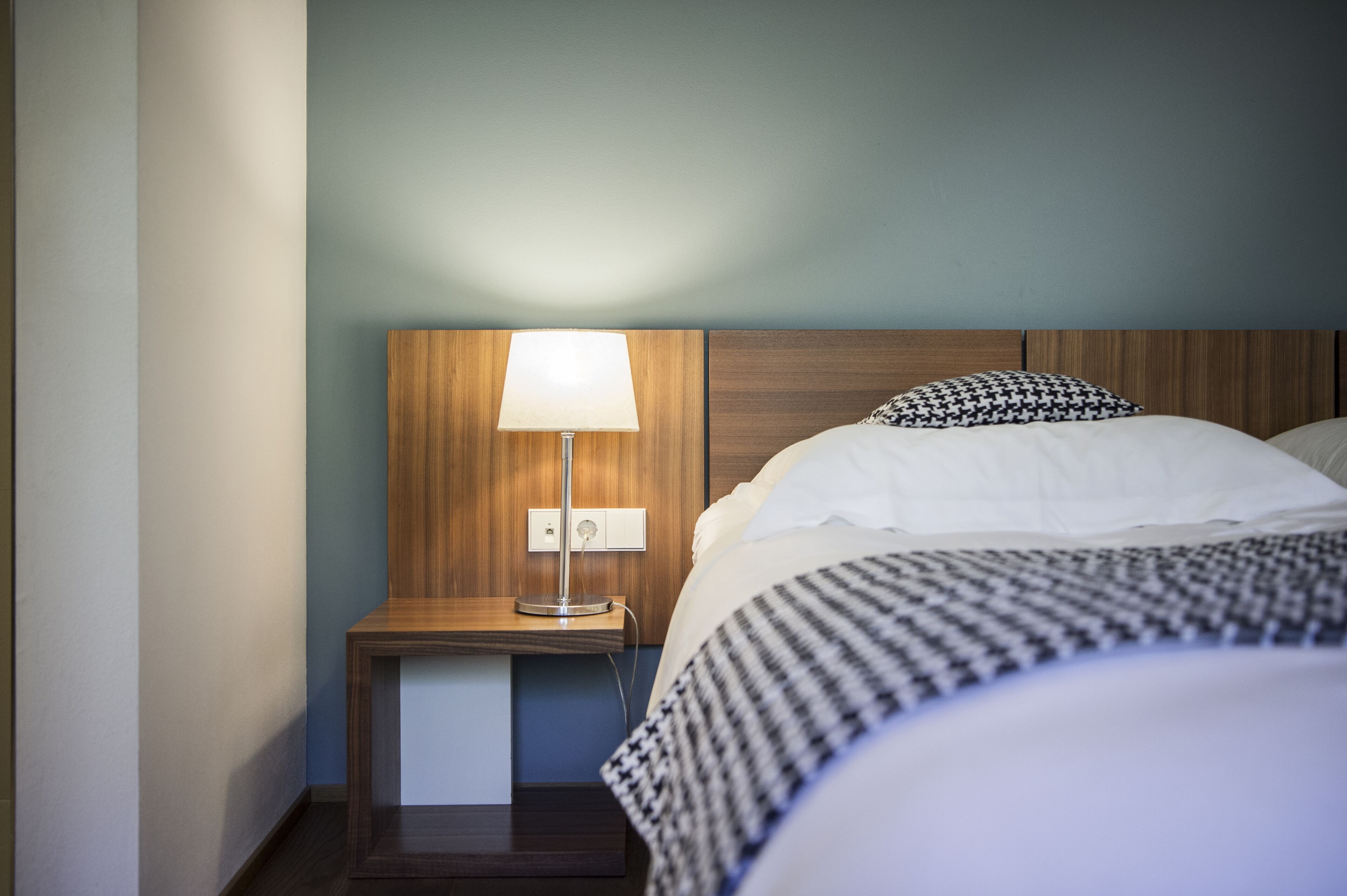 Een hotelkamer met een houten hoofdeinde, een bedlampje, een nachtkastje en een bed met gestreept beddengoed.