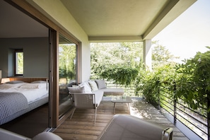 A modern bedroom with a large bed, a sofa, and a balcony with a view of greenery. - Designhotel Gius La Residenza (Caldaro Sulla Strada del Vino)