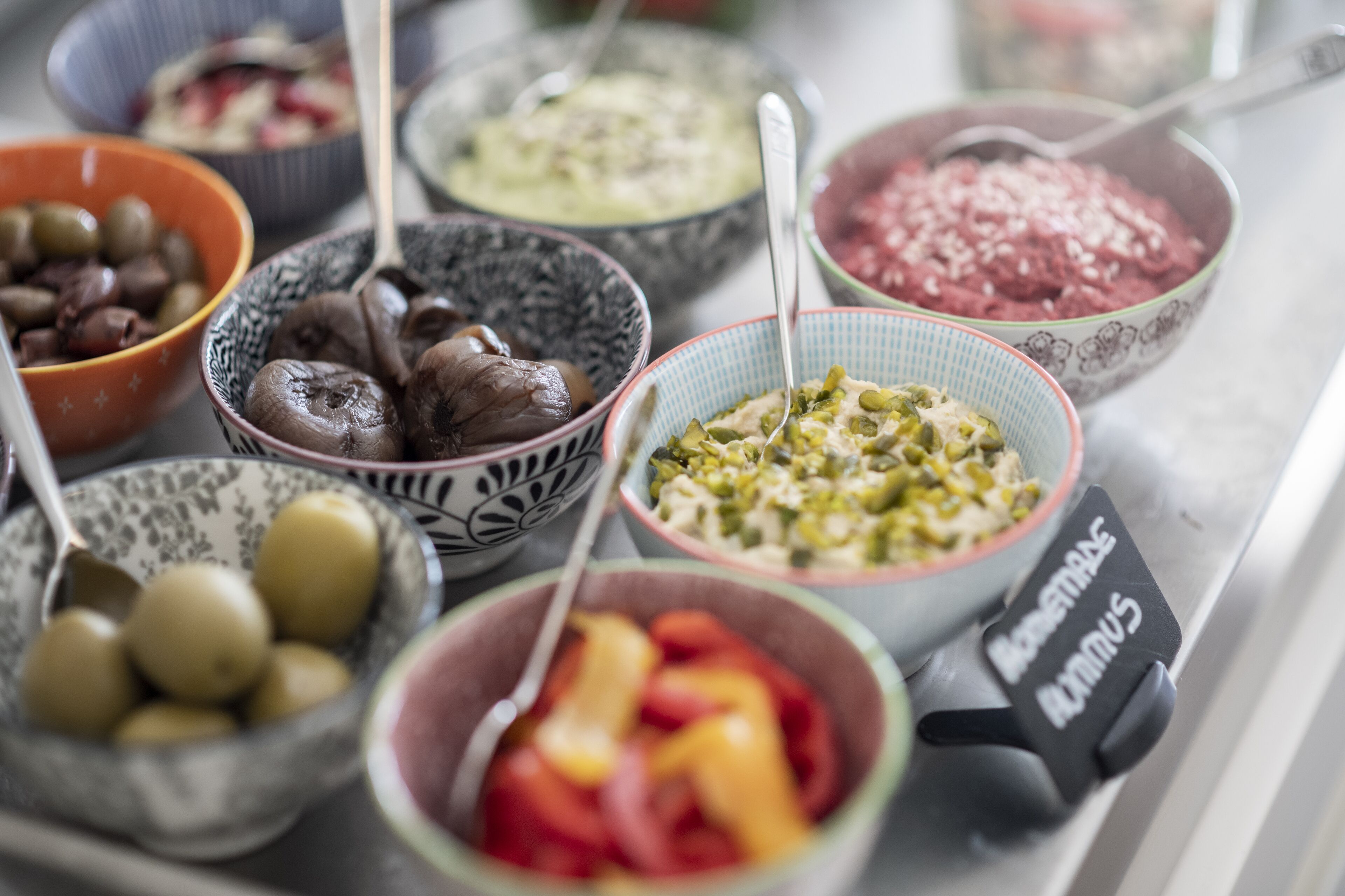 A variety of bowls with different foods, including olives, mushrooms, and a dish with green beans.
