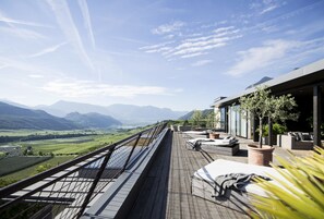 Um terraço com vista para montanhas, mesas ao ar livre e um deck de madeira.