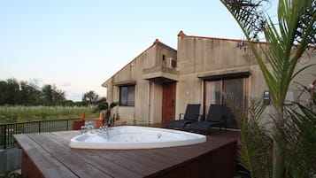 Relax on the deck with a hot tub and comfortable lounge chairs amidst lush greenery and a palm tree.