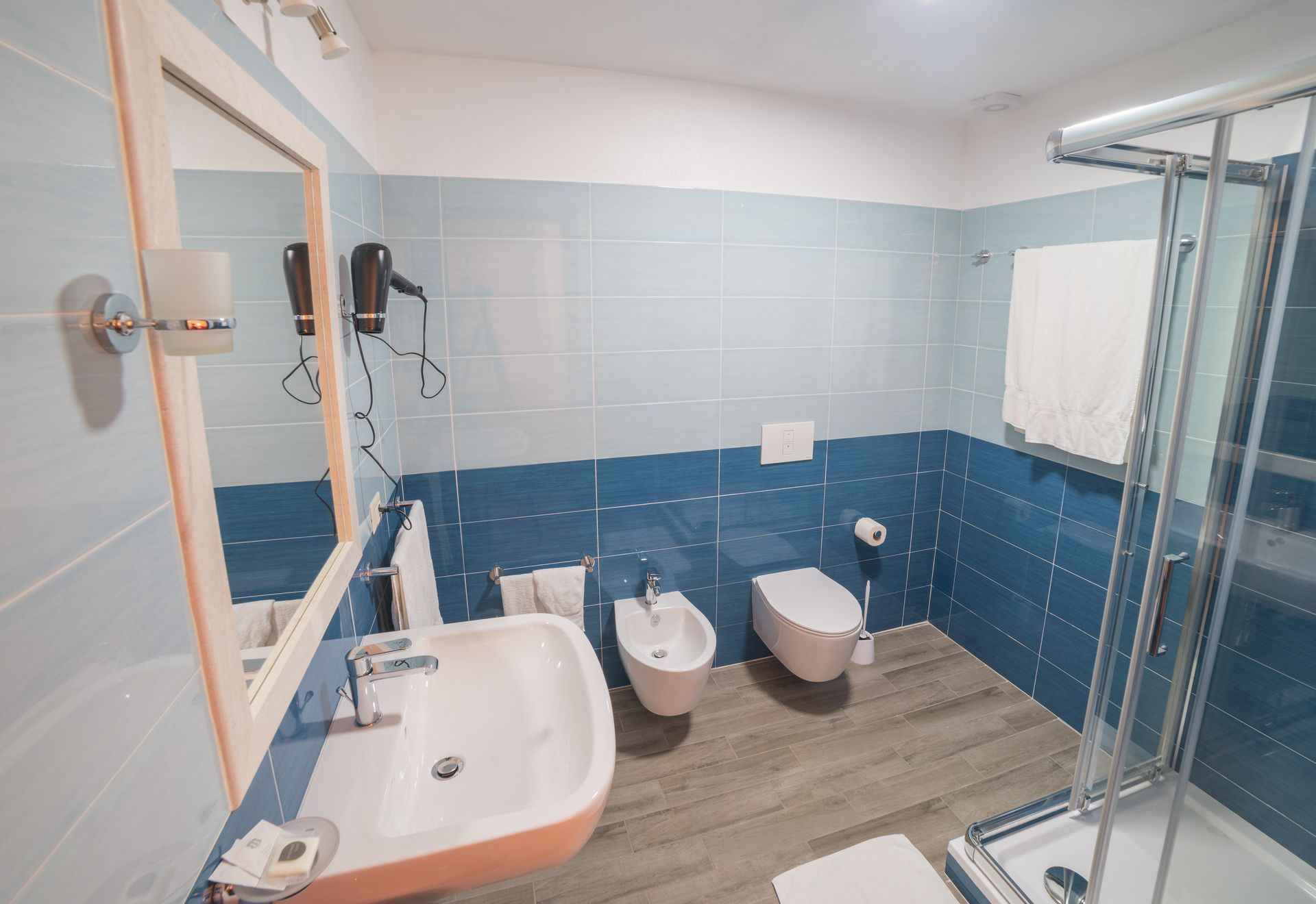 A bathroom with a sink, bidet, toilet, and a glass shower enclosure.