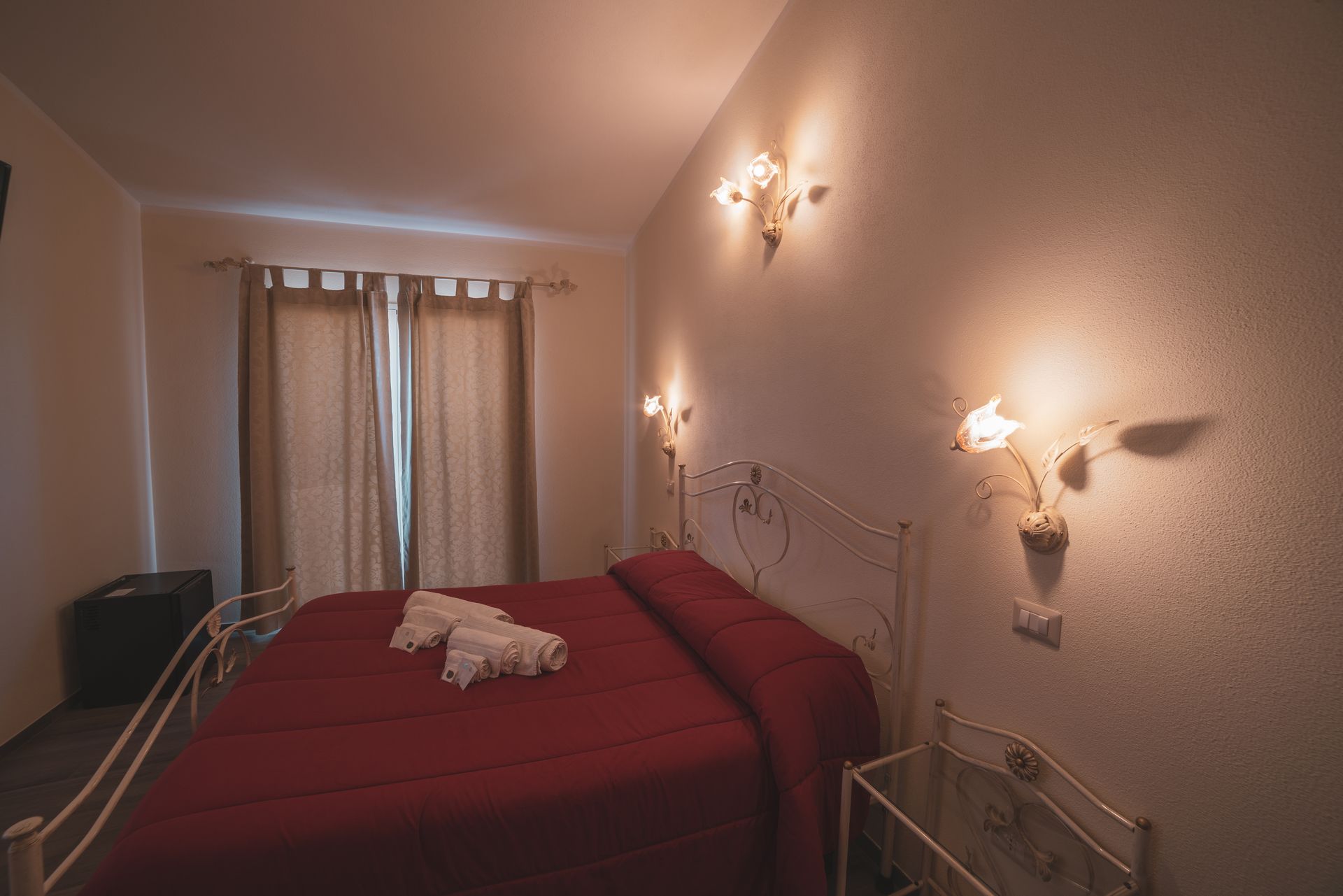 A hotel room with a bed, curtains, wall-mounted lights, and a radiator.